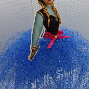 Puede incluir: Una falda de tul azul con purpurina, una botella de pl&aacute;stico transparente y una pegatina de Anna de Frozen con un lazo rosa. La pegatina dice "Lolli Store".