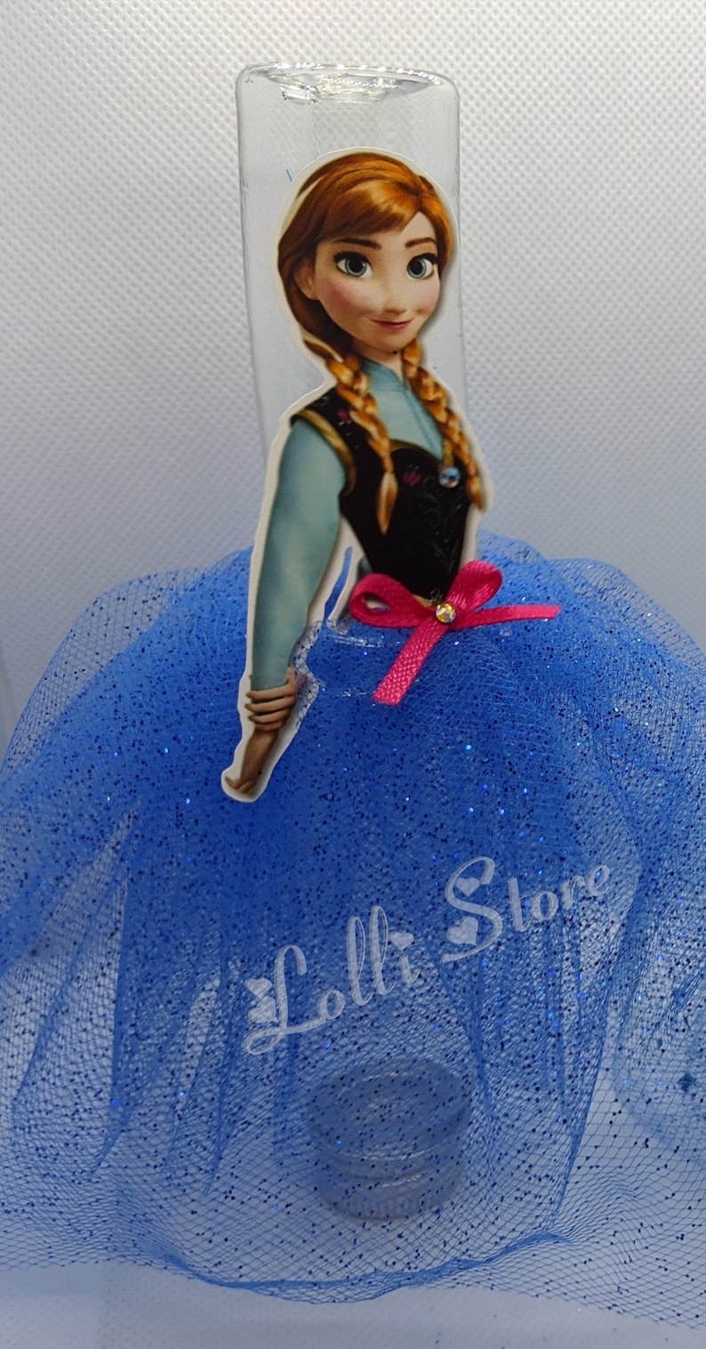 Puede incluir: Una falda de tul azul con purpurina, una botella de pl&aacute;stico transparente y una pegatina de Anna de Frozen con un lazo rosa. La pegatina dice "Lolli Store".