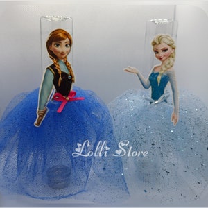 Puede incluir: Dos toppers de pastel de personajes de Frozen, uno con Anna y otro con Elsa. Ambos toppers llevan vestidos de tul azul con detalles de brillo. El texto "Lolli Store" es visible en la parte inferior central de la imagen.