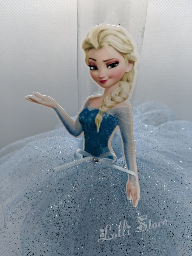Puede incluir: Una falda de tul azul claro con detalles de purpurina y un recorte de cart&oacute;n de Elsa de Frozen. El recorte muestra a Elsa con un vestido azul y una trenza.