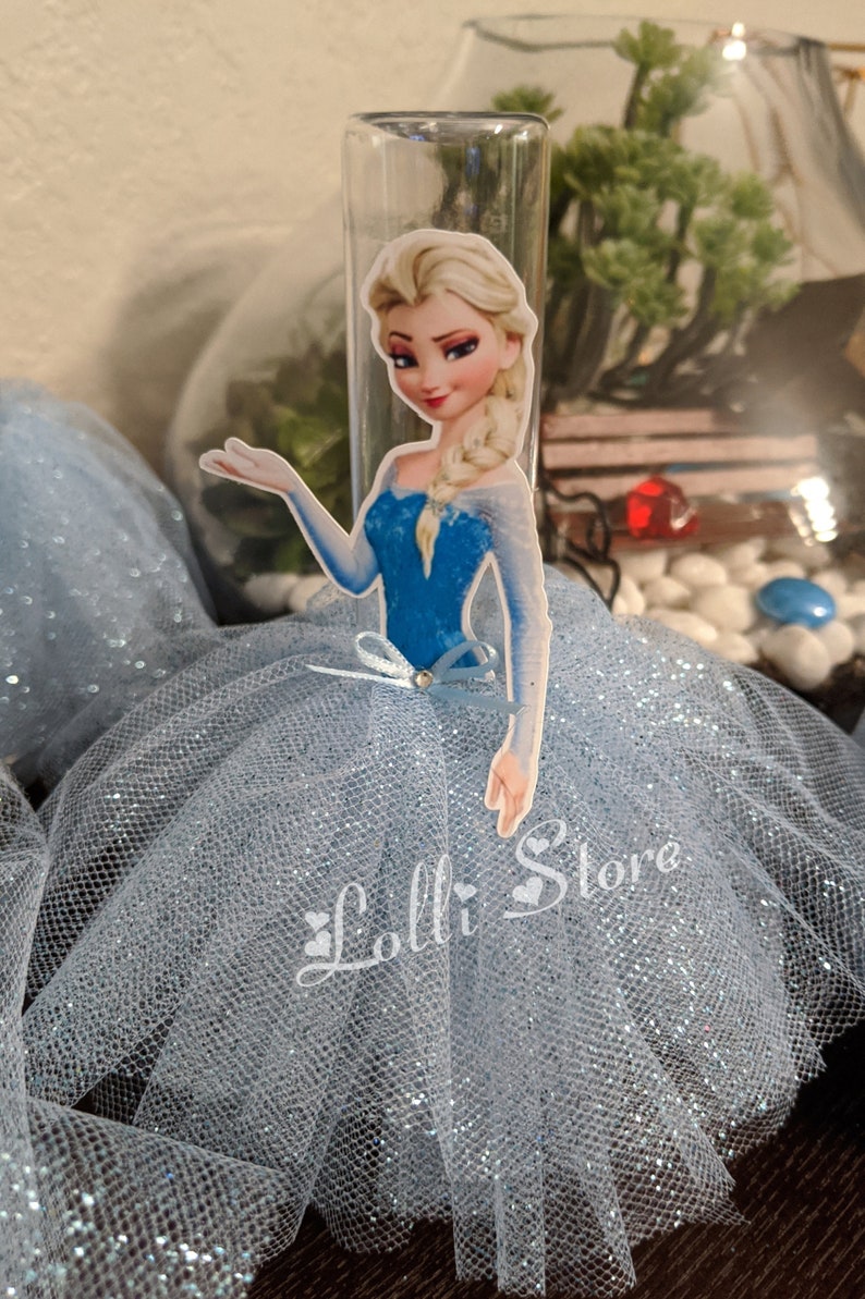 Puede incluir: Una falda de tul azul con detalles de purpurina y un recorte de Elsa de Frozen, con un vestido azul y una capa blanca, con la mano extendida. El texto "Lolli Store" es visible en la esquina inferior derecha de la imagen.