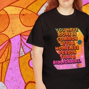 May include: Black t-shirt with the text "YOU HAVE MORE IN COMMON WITH A HOMELESS PERSON THAN A BILLIONAIRE" in a colorful, geometric design. The background is a retro-style pattern in orange, pink, and yellow.
