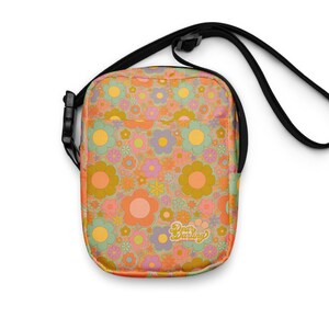 May include: A floral pattern crossbody bag with a black adjustable strap. The bag features a colorful retro floral design in shades of orange, pink, yellow, green, and purple. The text "Dear Darling" is printed on the front.