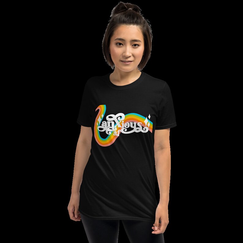 以下が含まれることがあります： 虹色のデザインで「Anxious af」の文字が入った黒いTシャツ。デザインは、虹色のアーチと星のアクセントが付いた、曲線的で様式化されたフォントが特徴です。このシャツは半袖のクルーネックです。