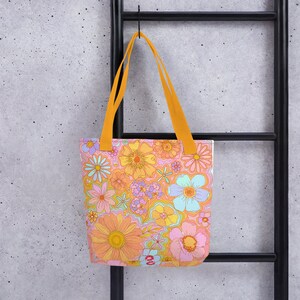 May include: A tote bag with a vibrant floral pattern in shades of orange, pink, yellow, and blue. The bag has bright orange handles and is hanging against a black metal ladder.