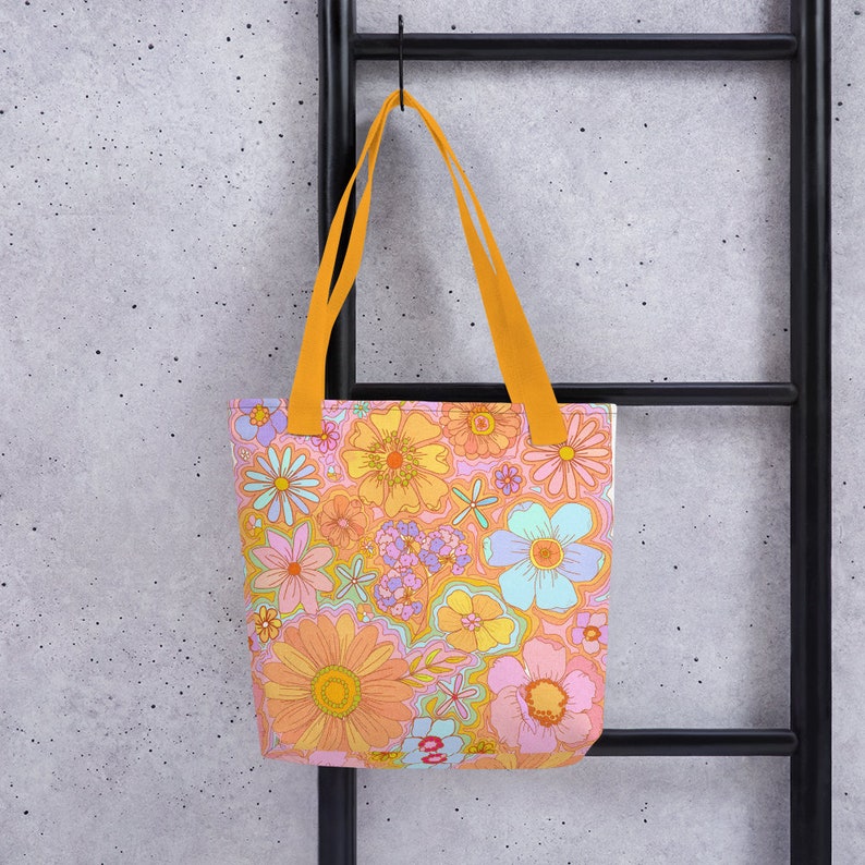 May include: A tote bag with a vibrant floral pattern in shades of orange, pink, yellow, and blue. The bag has bright orange handles and is hanging against a black metal ladder.