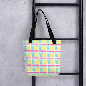 May include: A yellow tote bag with black straps and a repeating pattern of blue and pink squares with the text "OLD BAY" printed on each square.