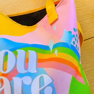 May include: A colorful tote bag with a rainbow design and the words "You are magic" in large white letters. The bag has yellow handles and a pink background with blue and green accents.