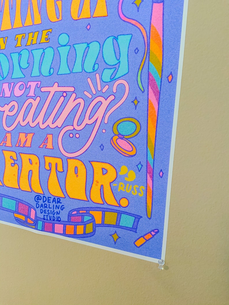 May include: A purple and blue poster with the text "If you're not creating in the morning, you're not a creator." The poster has a colourful design with stars, a film strip, and a makeup brush.
