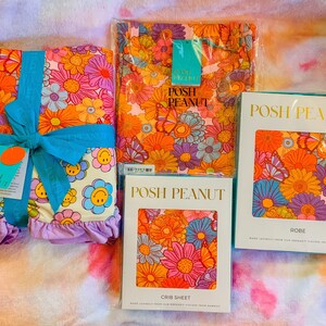 Puede incluir: Tres paquetes de ropa de cama y ropa con un estampado floral retro con mariposas y caritas sonrientes. Los paquetes est&aacute;n etiquetados como "Posh Peanut" e incluyen una s&aacute;bana de cuna, una bata y una manta.
