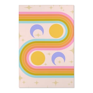 May include: A rectangular wall art print with a retro design. The artwork features a wavy, multi-colored stripe pattern in shades of orange, pink, blue, and yellow, with two yellow circles and two purple crescent moons. Gold star shapes are scattered across a light pink background.