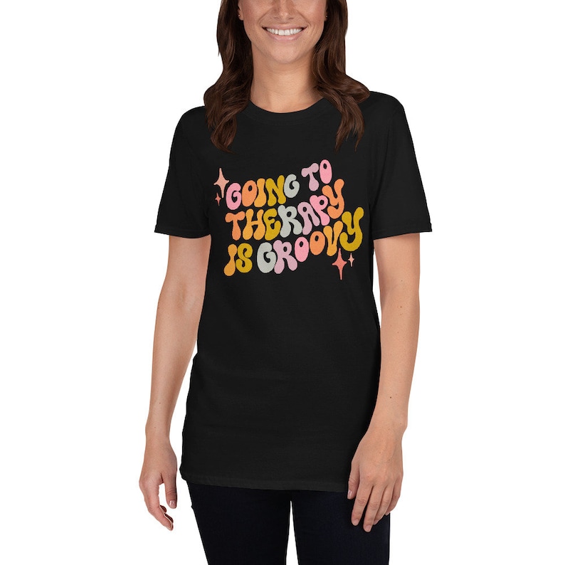 Puede incluir: Camiseta negra con un gr&aacute;fico de estilo retro que dice "Going to Therapy is Groovy" en letras coloridas y onduladas.
