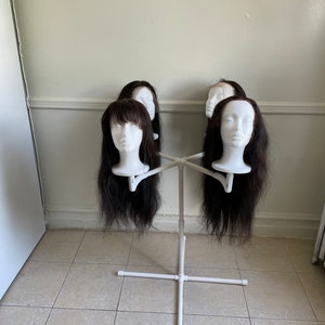 May include: A white wig stand with five black wigs on it. The stand has a white base and four arms that extend out to hold the wigs.