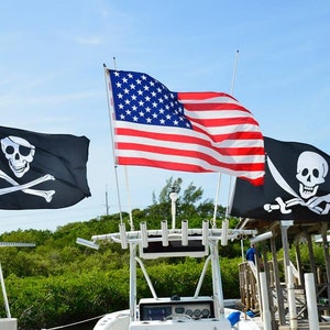 May include: Three flags flying in the wind. A black pirate flag with a white skull and crossbones, a black pirate flag with a white skull and crossbones and a sword, and an American flag.