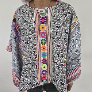 May include: A white poncho with a black geometric pattern and colorful floral embroidery along the front and sleeves.
