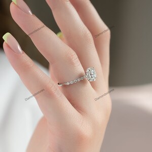 May include: A silver engagement ring with a large, round, clear gemstone. The band features small, round accent stones. The ring is on a person's finger.