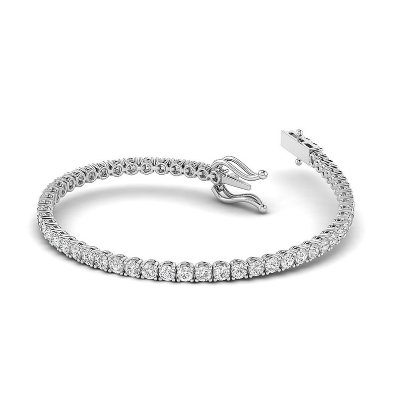 Puede incluir: Una pulsera de tenis con una fila de diamantes redondos engastados en metal blanco. La pulsera est&aacute; abierta, mostrando el mecanismo de cierre. Los diamantes brillan sobre el fondo blanco, creando un aspecto lujoso.