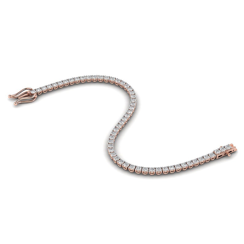 Puede incluir: Pulsera de tenis de oro rosa con una fila de diamantes redondos brillantes. La pulsera tiene un cierre seguro y se muestra sobre un fondo blanco. Una pieza de joyer&iacute;a cl&aacute;sica.