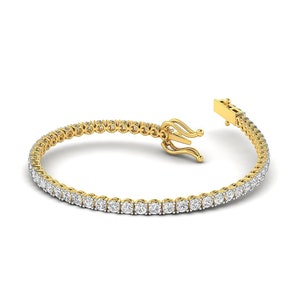 Puede incluir: Una pulsera de tenis dorada con una fila de piedras preciosas redondas y transparentes. La pulsera est&aacute; abierta, mostrando el cierre y el intrincado dise&ntilde;o del engaste de oro. Las piedras preciosas est&aacute;n espaciadas uniformemente y brillan.