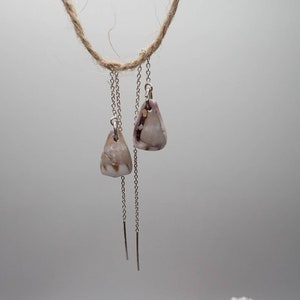 Puede incluir: Un par de pendientes de plata con pequeñas conchas triangulares colgando de los extremos.