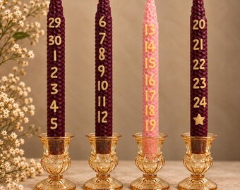 May include: Four tall, tapered beeswax candles with a honeycomb texture, each standing in a clear amber glass holder. Three candles are deep burgundy and one is light pink. Each candle features gold numbers marking dates.