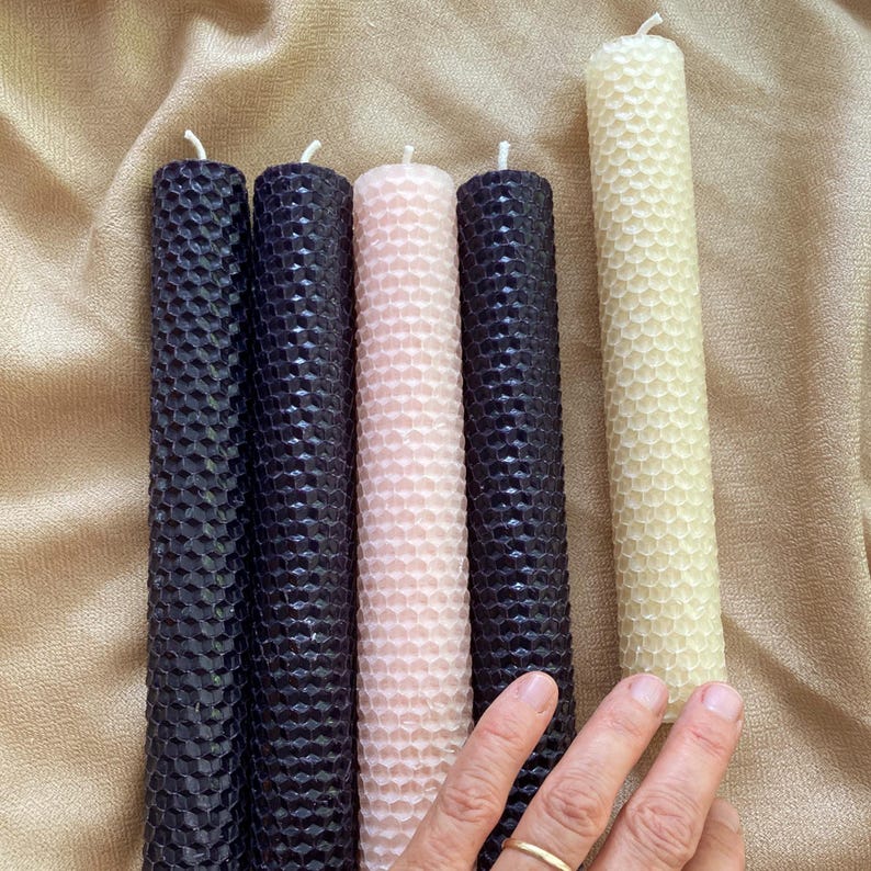 May include: Five cylindrical taper candles with a textured honeycomb pattern. The set includes three dark black candles, one soft pale pink candle, and one cream-colored candle. Each candle features a single white cotton wick at the top end.