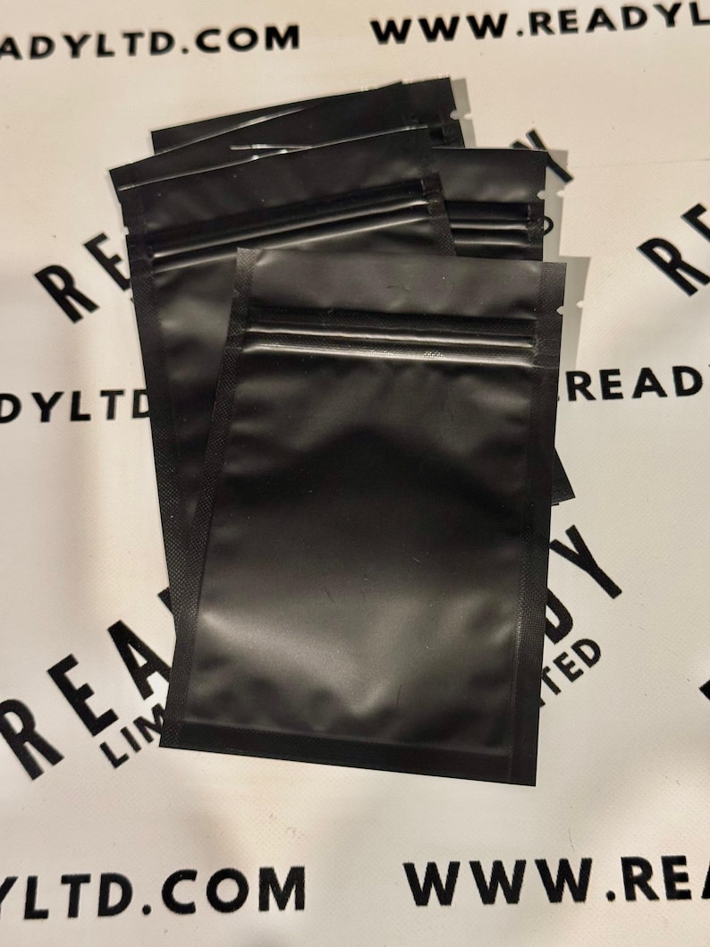 May include: A stack of five black zippered pouches with a silver zipper. The pouches are made of a shiny, smooth material.