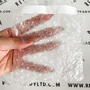 May include: A clear bubble wrap pouch with a white adhesive strip. The pouch is held by a hand with a light pink nail polish. The background has the text "READY LTD.COM" and "WWW.READYLTD.COM".