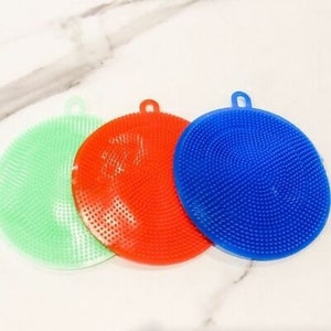 May include: Three colorful silicone dish scrubbers. One is green, one is red, and one is blue. Each scrubber is round with a textured surface and a small loop for hanging. The scrubbers are designed for kitchen use.