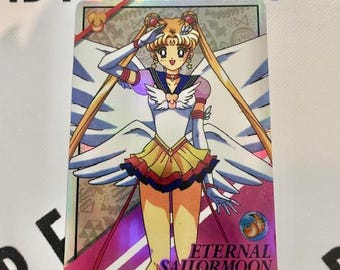 Puede incluir: Tarjeta coleccionable holográfica con Eternal Sailor Moon. La tarjeta muestra un personaje con un atuendo blanco, rosa y dorado con grandes alas. La tarjeta tiene el texto "Eternal Sailor Moon" y texto japonés.