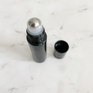 Könnte beinhalten: Eine schwarze Rollflasche mit einer silbernen Rollkugel. Die Flasche steht auf einer weißen Marmorfläche.