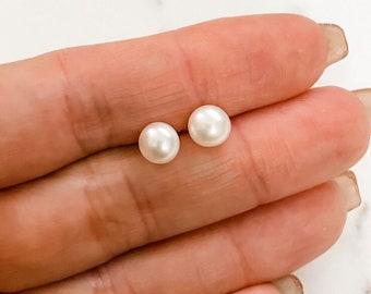 Op de afbeelding: Een paar parel oorbel studs. De oorbellen zijn klein en rond, en ze zijn een klassieke witte kleur.