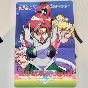 Könnte beinhalten: Eine Sailor Moon SuperS Sammelkarte mit drei Anime-Charakteren. Die Karte hat einen blauen Hintergrund mit dem Text "SAILOR MOON SuperS" und japanischem Text. Die Charaktere sind in verschiedenen Posen mit leuchtenden Farben.