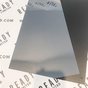 May include: A clear, translucent sheet of plastic with a slightly textured surface. The sheet is lying on top of a black sheet of paper. The text "READY LIMITED" is printed on the plastic sheet.