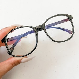 May include: Black square-shaped glasses with clear lenses and a black frame.