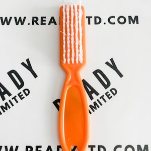 Puede incluir: Un cepillo de uñas naranja con cerdas blancas. El cepillo tiene un mango con un agujero en el extremo. El texto "READY LIMITED" y "WWW.READY.TD.COM" está impreso en el fondo.