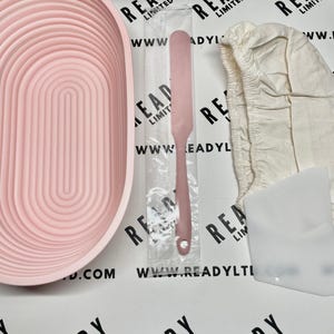 Pode incluir: Um conjunto de pastelaria em silicone rosa, incluindo uma tigela, uma espátula, um raspador de massa e um pano de linho. A tigela tem um design arqueado único. A espátula e o raspador também são rosa. O conjunto é projetado para assar.