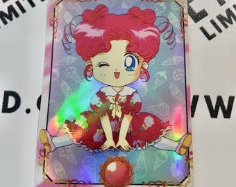 Puede incluir: Tarjeta coleccionable holográfica con un personaje de dibujos animados con pelo rosa y un vestido rojo. La tarjeta tiene un borde rosa y dorado y el texto "CHIBICHIBI" y caracteres japoneses.
