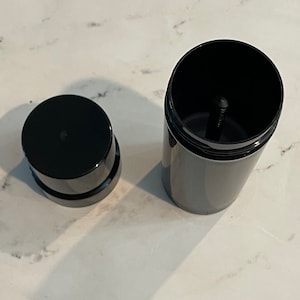 Könnte beinhalten: Ein schwarzer Plastikbehälter mit einem Schraubverschluss. Der Behälter ist offen und der Deckel ist abgenommen. Der Behälter ist leer.
