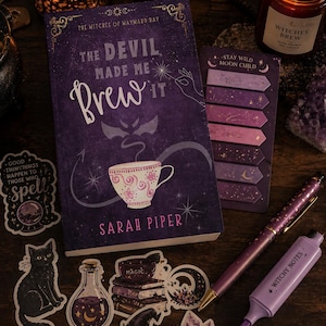 May include: A book titled The Devil Made Me Brew It by Sarah Piper with a purple cover featuring a teacup, a set of purple sticky notes labelled Stay Wild Moon Child, a purple pen, a purple highlighter labelled Witchy Notes, and various stickers.