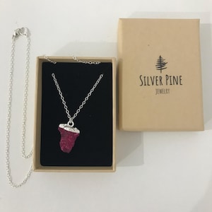 May include: A silver chain necklace with a pink and silver pendant in a black box. The box is labelled "Silver Pine Jewelry".