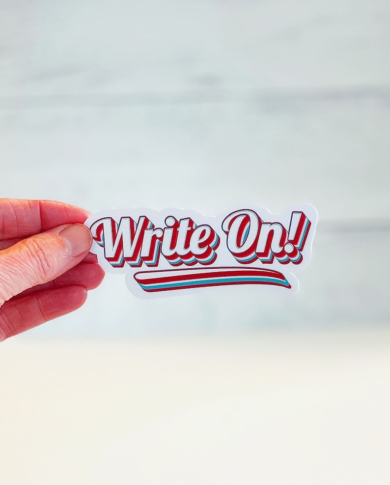 以下が含まれることがあります： 白いステッカーに「Write On!」という文字が赤と青の文字で書かれており、白いアウトラインがあります。文字はレトロなスタイルのフォントです。