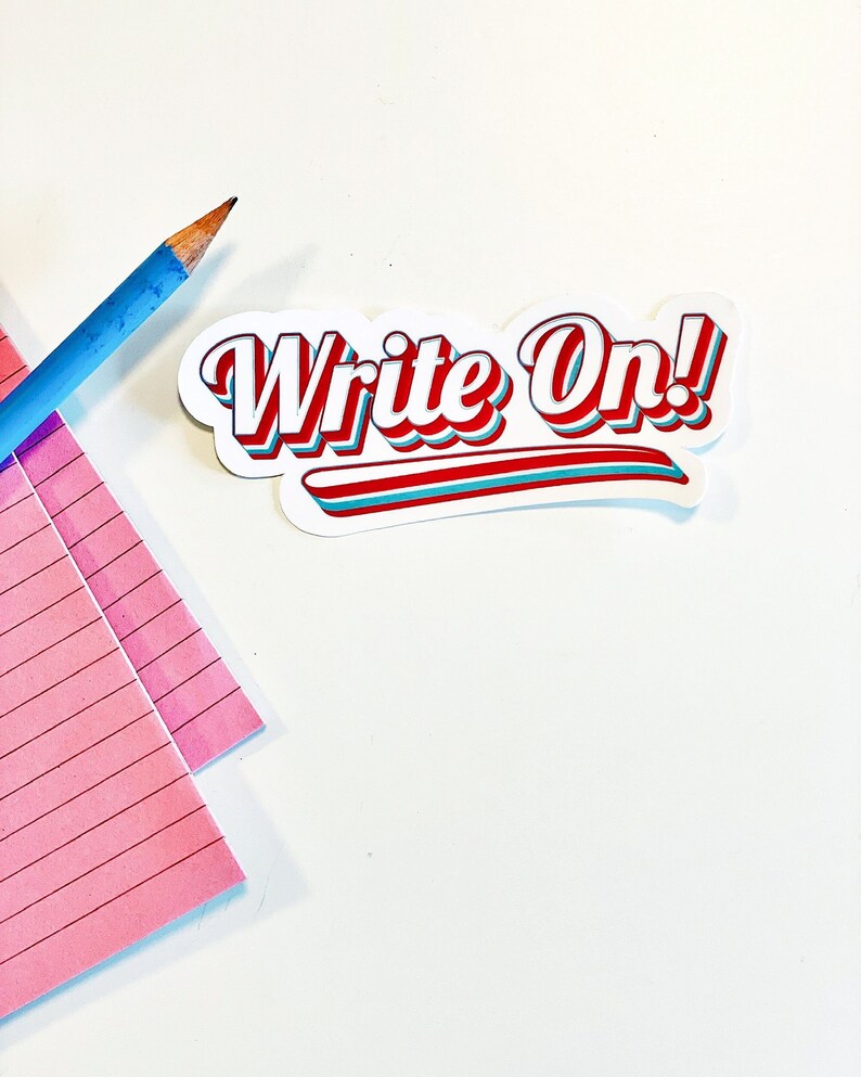 以下が含まれることがあります： 白地に「Write On!」という赤い、青い、白いレトロな文字が書かれたステッカー。ステッカーは、ピンクの罫線のあるメモ帳と青い鉛筆のある白い表面に置かれている。