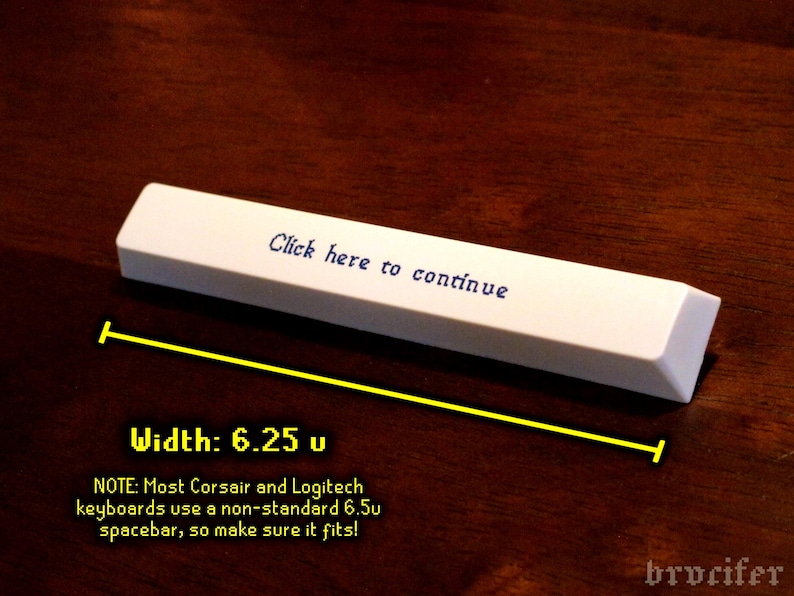 K&ouml;nnte beinhalten: Eine wei&szlig;e Tastatur-Leertaste mit dem Text "Click here to continue". Die Leertaste ist 15,88 cm breit. Das Bild befindet sich auf einer dunkelbraunen Oberfl&auml;che.