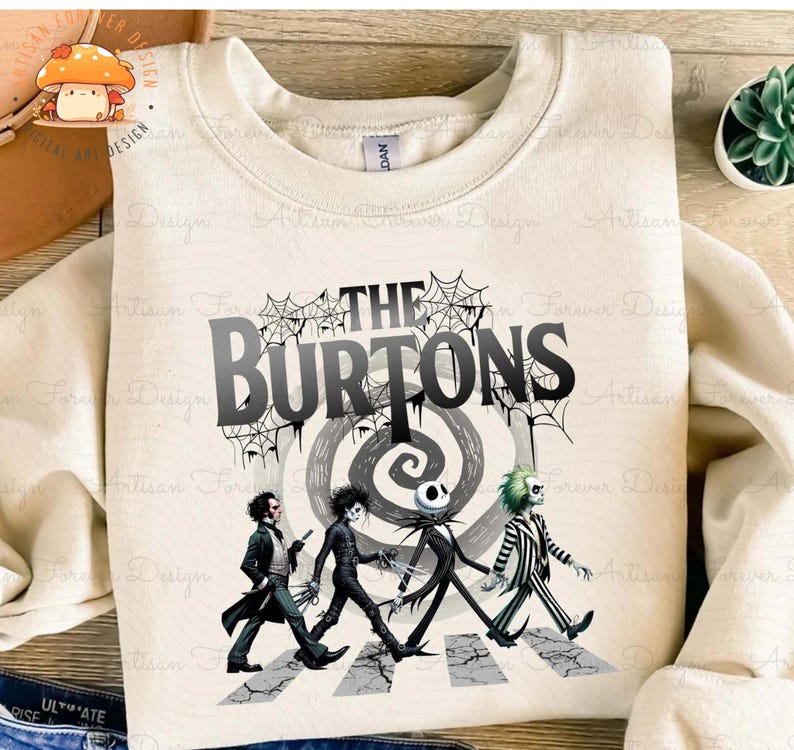 May include: A beige sweatshirt with a graphic print of characters from The Nightmare Before Christmas and Beetlejuice walking across a crosswalk. The text "The Burtons" is printed above the characters.