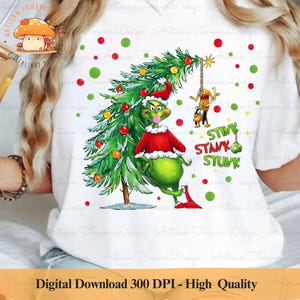 Puede incluir: Una camiseta blanca con un personaje verde del Grinch sosteniendo un árbol de Navidad. El Grinch lleva un gorro de Papá Noel rojo y una camisa roja. El texto "STINK STANK STUNK" está impreso en la camiseta.