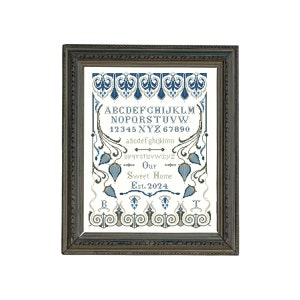 May include: A framed cross-stitch sampler with a blue and green color scheme. The sampler features an alphabet, numbers, and the text "Our Sweet Home Est. 2024".
