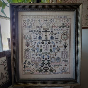 Puede incluir: Un sampler enmarcado con fondo blanco y bordado negro. El sampler presenta un alfabeto, números y una variedad de diseños florales y geométricos. El texto "A Niece's  Embroidered  Sampler To Her  1810" está en la parte superior del sampler.