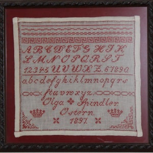 May include: A framed sampler with red embroidery on white linen. The sampler includes the alphabet, numbers, and the name "Olga Spindeler" with the date "1897".