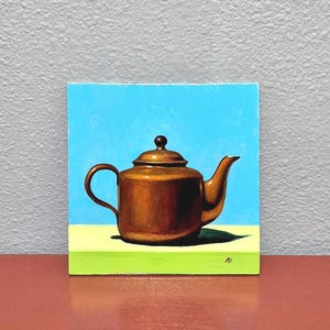 Puede incluir: Una pintura cuadrada que muestra una tetera de color cobre metálico centrada sobre un fondo azul brillante. La tetera descansa sobre una superficie plana de color verde claro. Las iniciales AD son visibles en la esquina inferior derecha.